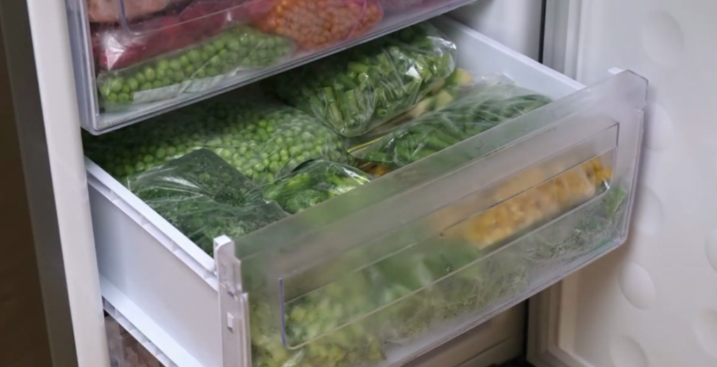 an open crisper drawer with veggies stored in transparent silicone bags